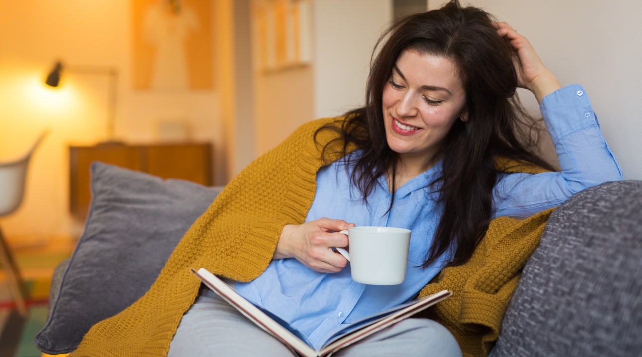 A woman on the couch with a cup of tea and a book